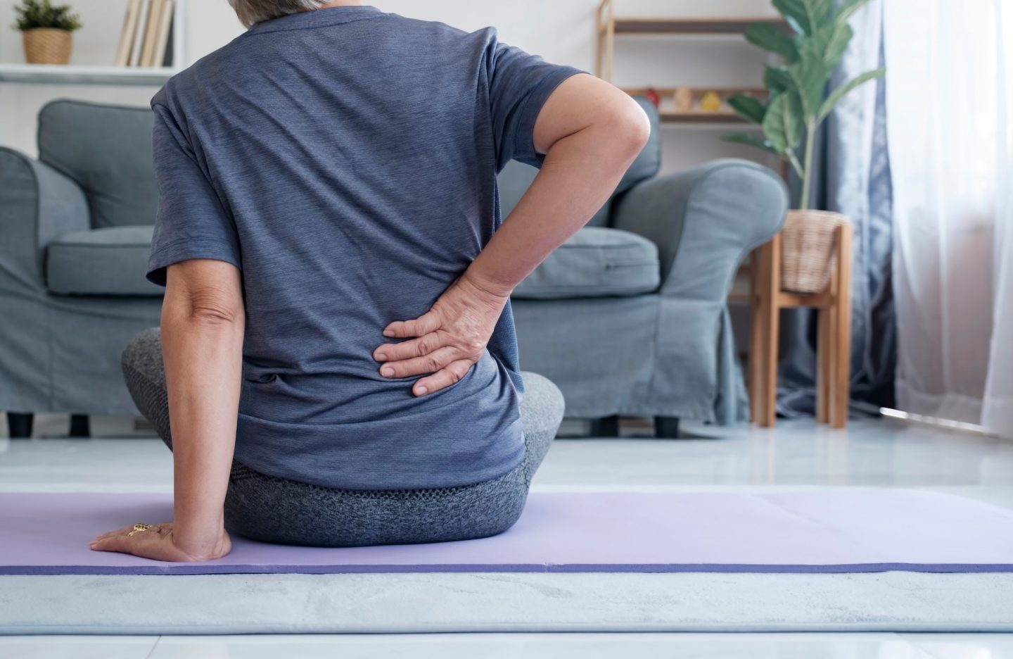 Elderly woman with back pain holding her lower back.